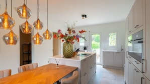 Una cocina moderna con una isla central, luces colgantes y un jarrón con flores.