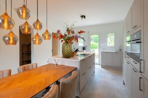 Eine moderne Küche mit einer zentralen Kochinsel, Pendelleuchten und einem Blumenstrauß.