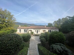 Ein zweistöckiges Haus mit Ziegeldach, umgeben von gepflegten Hecken und einem Steinweg, der zum Eingang führt.