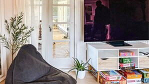 A living room with a television, a sofa, a potted plant, and a bookshelf with puzzle games. - 4 bedroom awesome home in Slagelse (Slagelse)