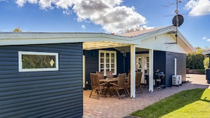 A small, dark-colored house with a patio area featuring a table and chairs, a grill, and a satellite dish. - 4 bedroom awesome home in Slagelse (Slagelse)