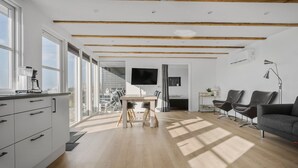 Un interno moderno con cucina, zona pranzo e soggiorno, caratterizzato da travi in legno, ampie finestre e una televisione a schermo piatto.