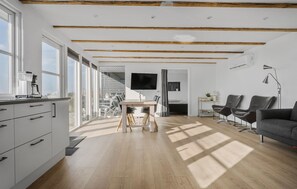 A modern interior with a kitchen, dining area, and living space, featuring wooden beams, large windows, and a flat-screen TV. - Lovely home in Slagelse with house sea view (Slagelse)