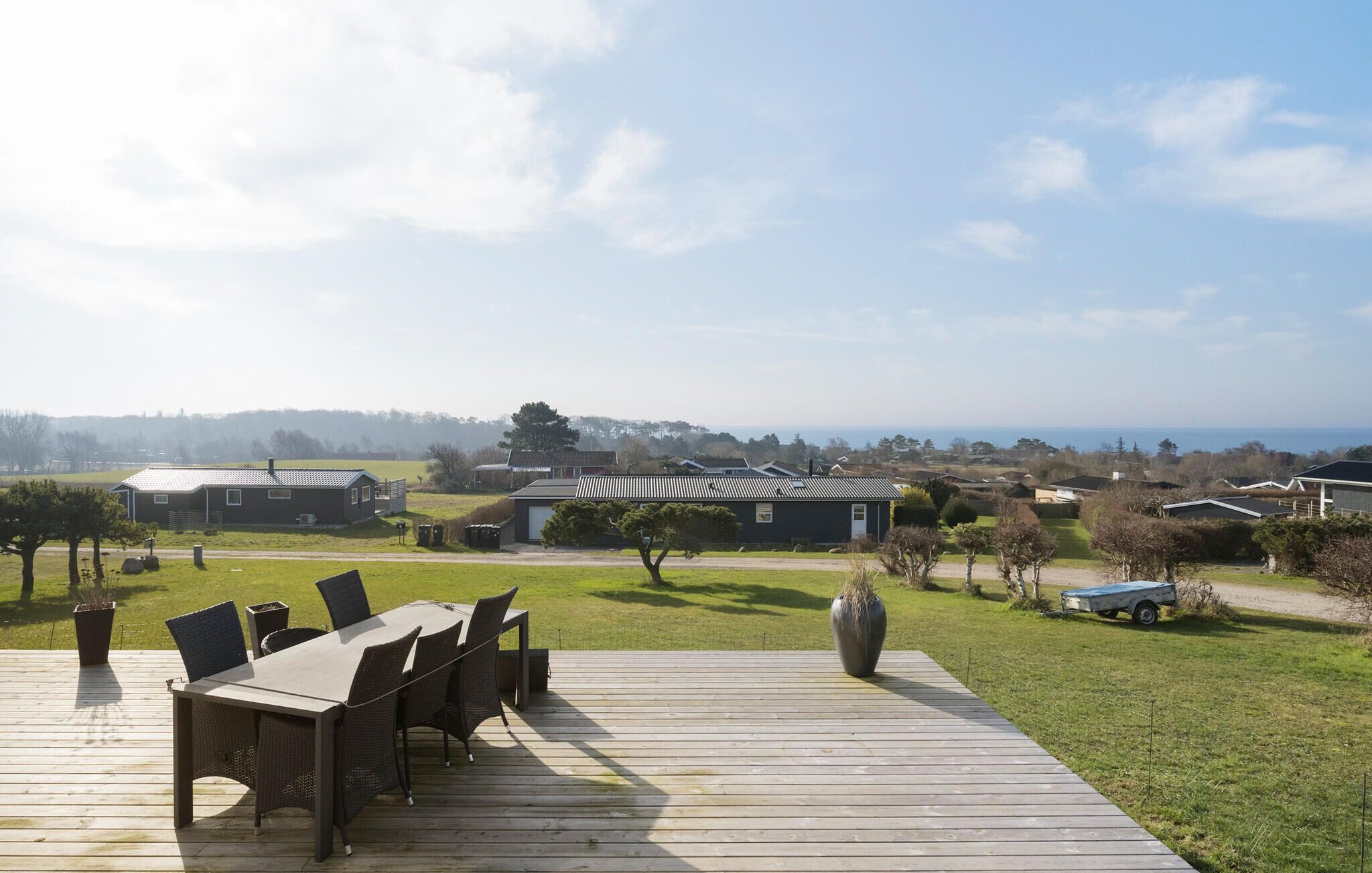 A deck with a table and chairs, a large planter, and a view of houses and the sea.