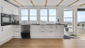 Una cucina moderna con mobili bianchi, forno integrato, macchina del caffè e ampie finestre con vista sull'esterno.