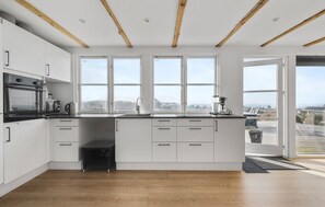 A modern kitchen with white cabinets, a built-in oven, a coffee machine, and large windows offering a view of the outside. - Lovely home in Slagelse with house sea view (Slagelse)