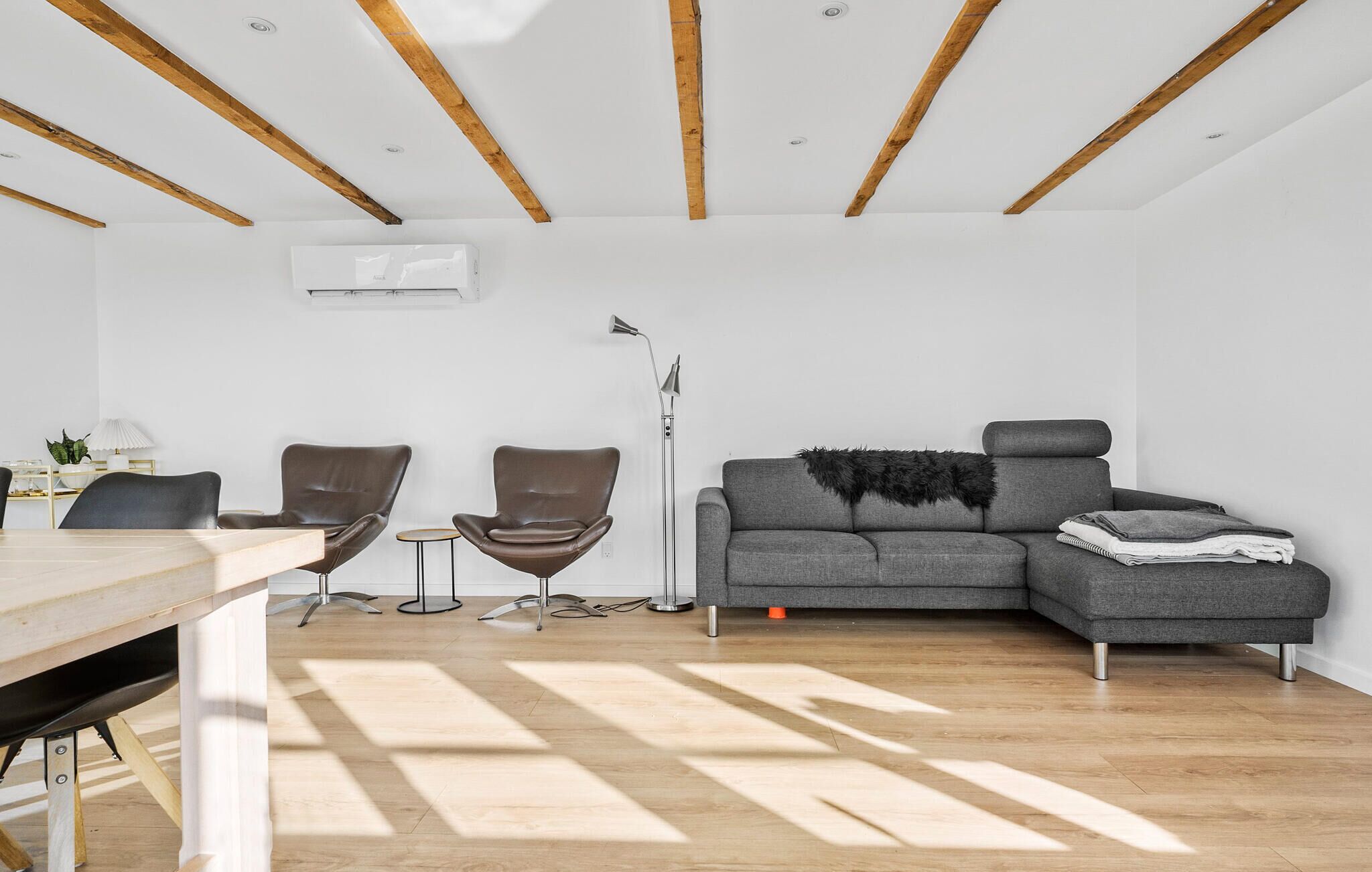 A modern living room with a grey sofa, two brown chairs, a wooden dining table, and a floor lamp.