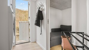 Un corridoio stretto con una porta che dà all'esterno, un divano grigio e una giacca nera appesa al muro.