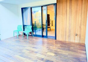 Ein Zimmer mit Holzboden, einer Schiebeglastür, die auf einen Balkon führt, und zwei grünen Stühlen.