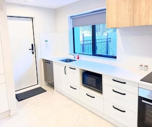 Eine moderne Küche mit weißen Schränken, einem Einbauofen, einer Spüle und einem Fenster mit Blick ins Freie.