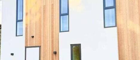 A modern building with a white facade and wooden accents, featuring a door and windows.