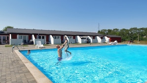 Une piscine avec une terrasse carrelée, des chaises longues et un bâtiment avec un toit rouge en arrière-plan.
