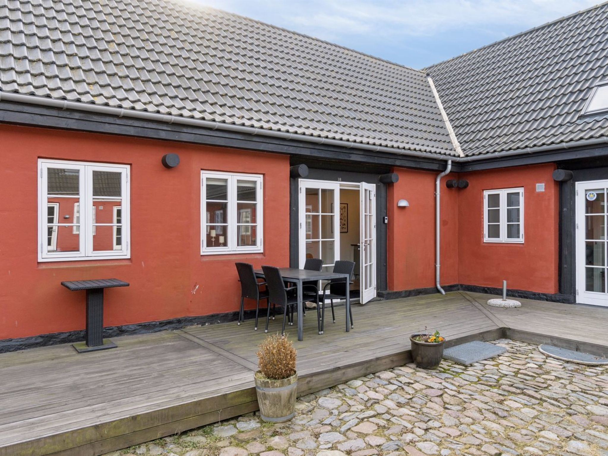Ein Gebäude mit Ziegeldach, einer Holzterrasse und einem kleinen Garten mit einem Blumentopf.