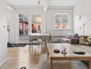Ein modernes Wohnzimmer mit Essbereich, einer Couch, einem Couchtisch und Blick auf ein rotes Gebäude durch die Glastür.