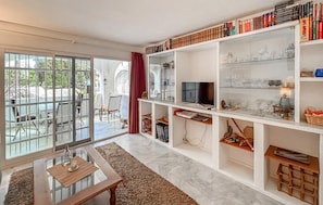 Ein modernes Wohnzimmer mit einem Glastisch, einem Fernseher und Bücherregalen voller Bücher und Dekorationsgegenstände.
