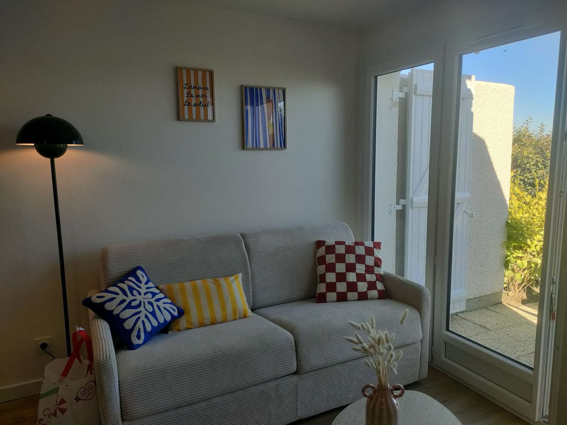 A living room with a sofa, pillows, a floor lamp, and a vase with dried flowers.