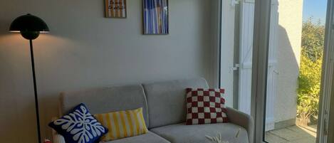 A living room with a sofa, pillows, a floor lamp, and a vase with dried flowers.