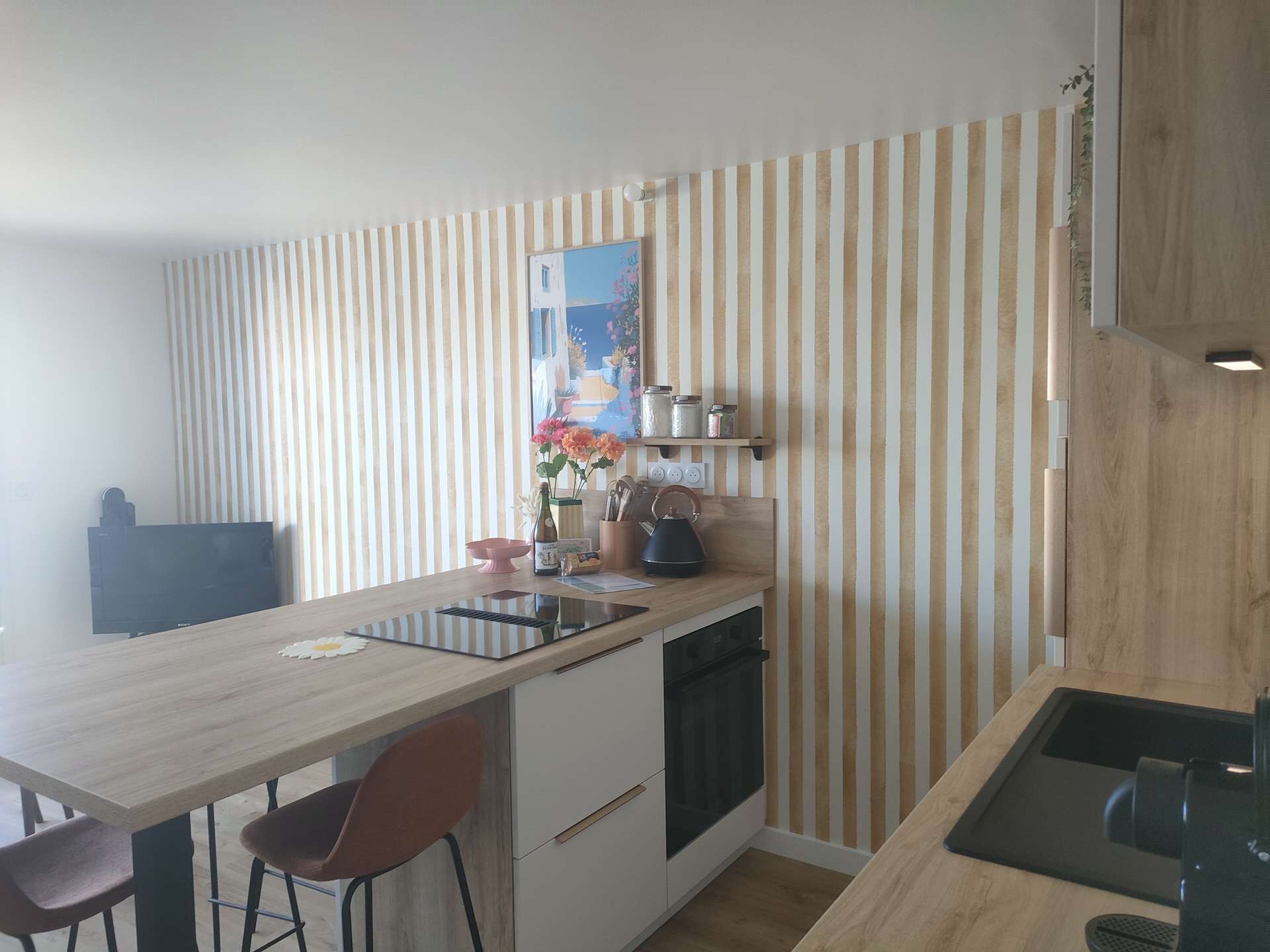 Ett kök med en randig vägg, en liten köksö, en diskmaskin och en tv.
