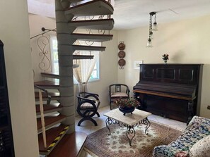 A living room with a piano, a staircase, a table with a vase, and a patterned rug. - Casa Floripa - Praia Daniela, 5-7 pessoas, 300m da Praia - 4 Estacoes (Florianópolis)