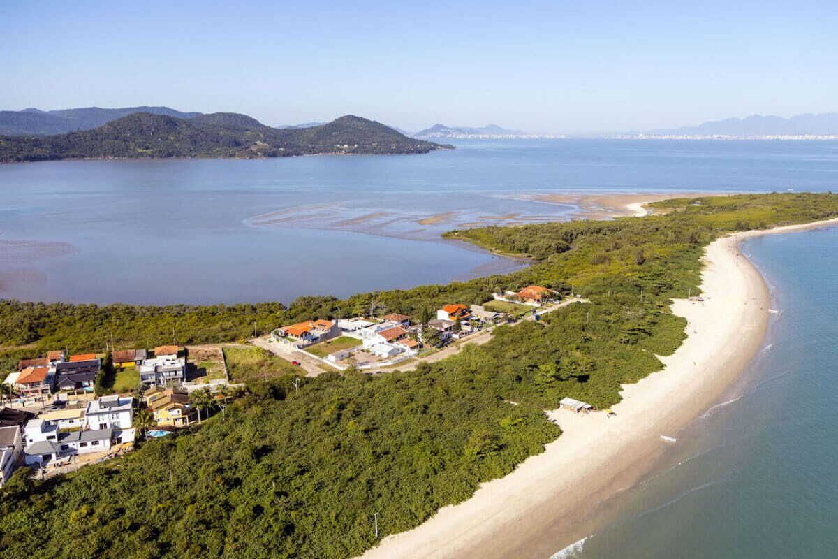 An aerial view of a coastal area with a beach, a small settlement, and hills in the background.