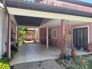 A covered patio with tiled flooring, potted plants, and a door with a window. - Casa Floripa - Praia Daniela, 5-7 pessoas, 300m da Praia - 4 Estacoes (Florianópolis)