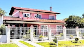 A two-story house with a red-tiled roof, a gated entrance, and a small garden. - Casa Floripa - Praia Daniela, 5-7 pessoas, 300m da Praia - 4 Estacoes (Florianópolis)