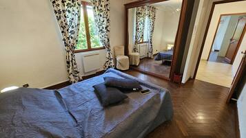 Ein Schlafzimmer mit Bett, Spiegel, Fenster mit Vorhängen und Heizkörper.