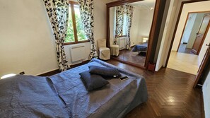 Ein Schlafzimmer mit Bett, Spiegel, Fenster mit Vorhängen und Heizkörper.