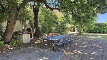 Un patio al aire libre con mesa y sillas, una parrilla y una pérgola.