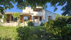 Ein zweistöckiges Haus mit verdeckter Veranda, einer Steintreppe und einem Garten mit verschiedenen Pflanzen und Sträuchern.