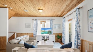 A living room with a wooden ceiling, a television, a sofa, a coffee table, and curtains.