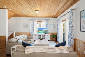 Ein Wohnzimmer mit Holzboden, einem Fernseher, einem Sofa, einem Couchtisch und Vorhängen.