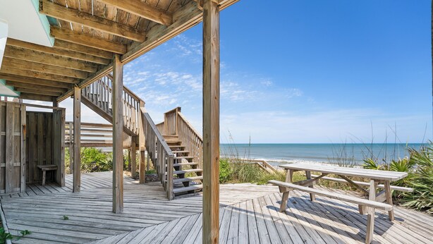 A wooden deck with a picnic table and stairs leading to a beach.