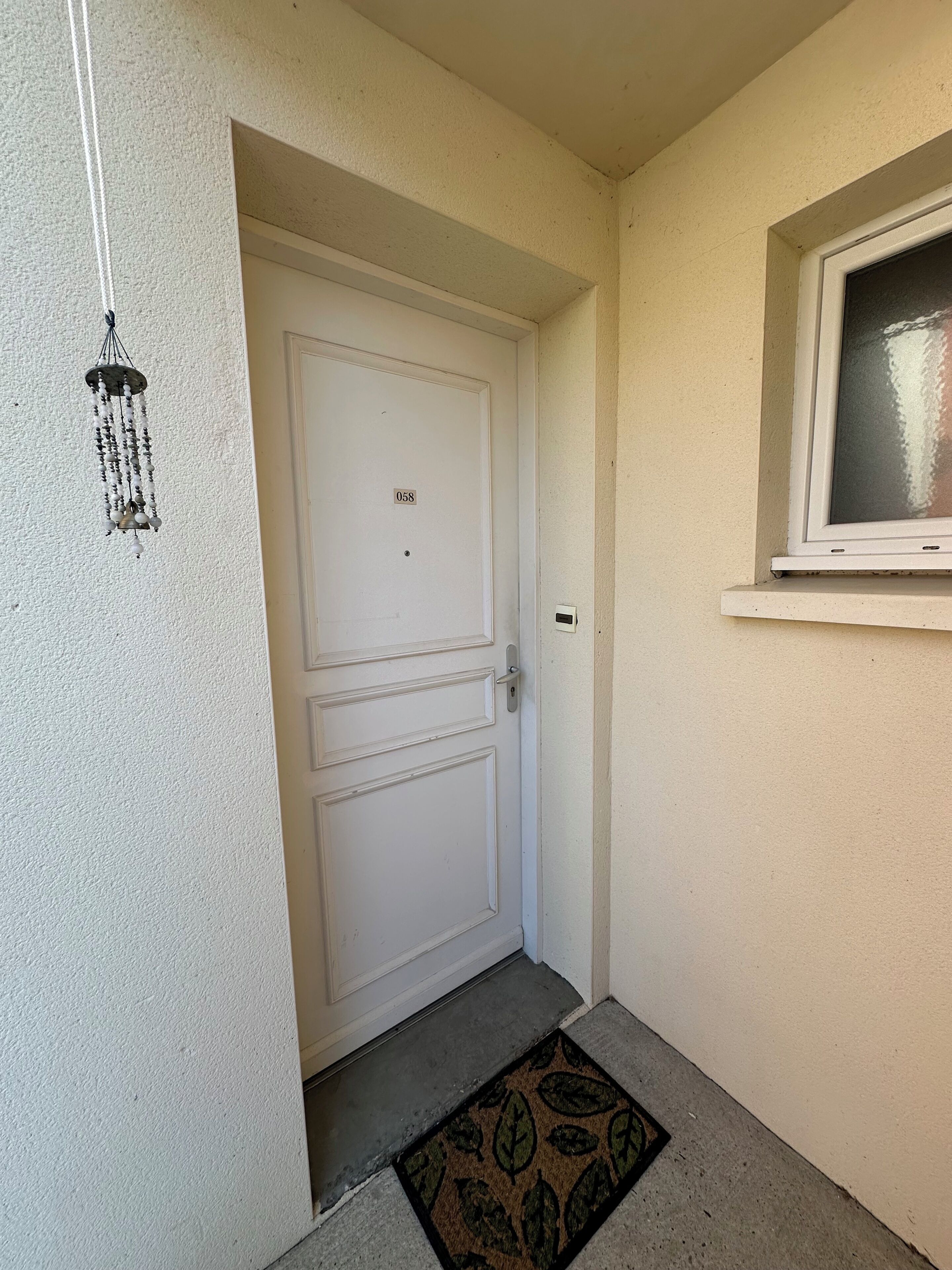Une porte blanche avec une plaque portant un numéro, une petite fenêtre et un sonnette.