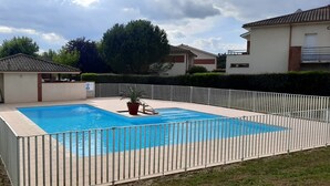 A rectangular swimming pool with a white fence, surrounded by a grassy area and a small pavilion.