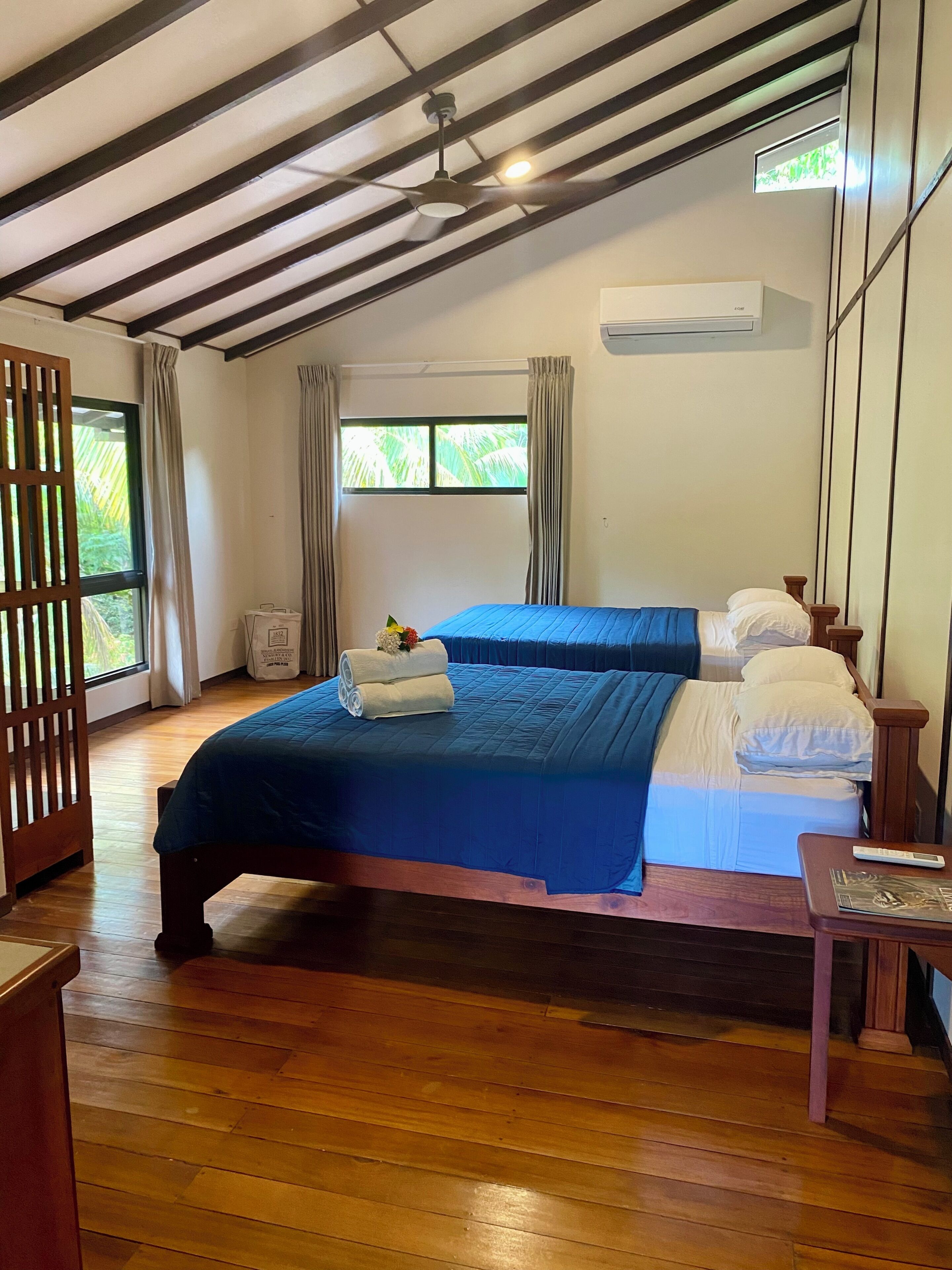 A room with a bed, a wooden floor, a ceiling fan, and a window with curtains.