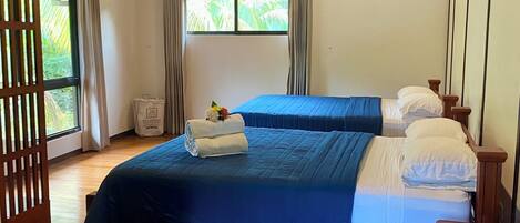 A room with a bed, a wooden floor, a ceiling fan, and a window with curtains.