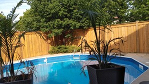 Ein Schwimmbecken mit Holzzaun, Topfpflanzen und blauem Himmel.