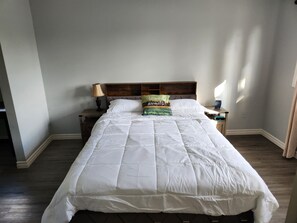A neatly made bed with a white comforter and pillows, a wooden headboard, a bedside lamp, and a small table with a lamp. - CasaLoma Private Oasis, minutes from the YYZ airport. (LIC 2026-005872-STA) (Mississauga)