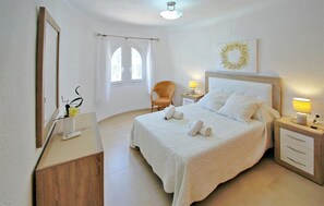 Ein ordentlich eingerichtetes Hotelzimmer mit Bett, Nachttischen, einem Sessel, einem Spiegel und einem Fenster mit Vorhängen.