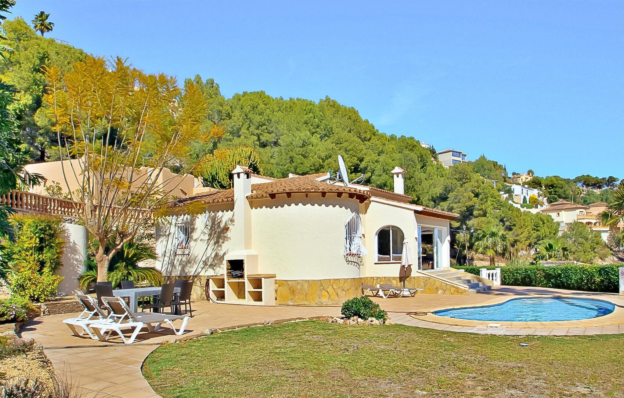 A Mediterranean-style villa with a swimming pool, outdoor seating, and a view of the surrounding hills.