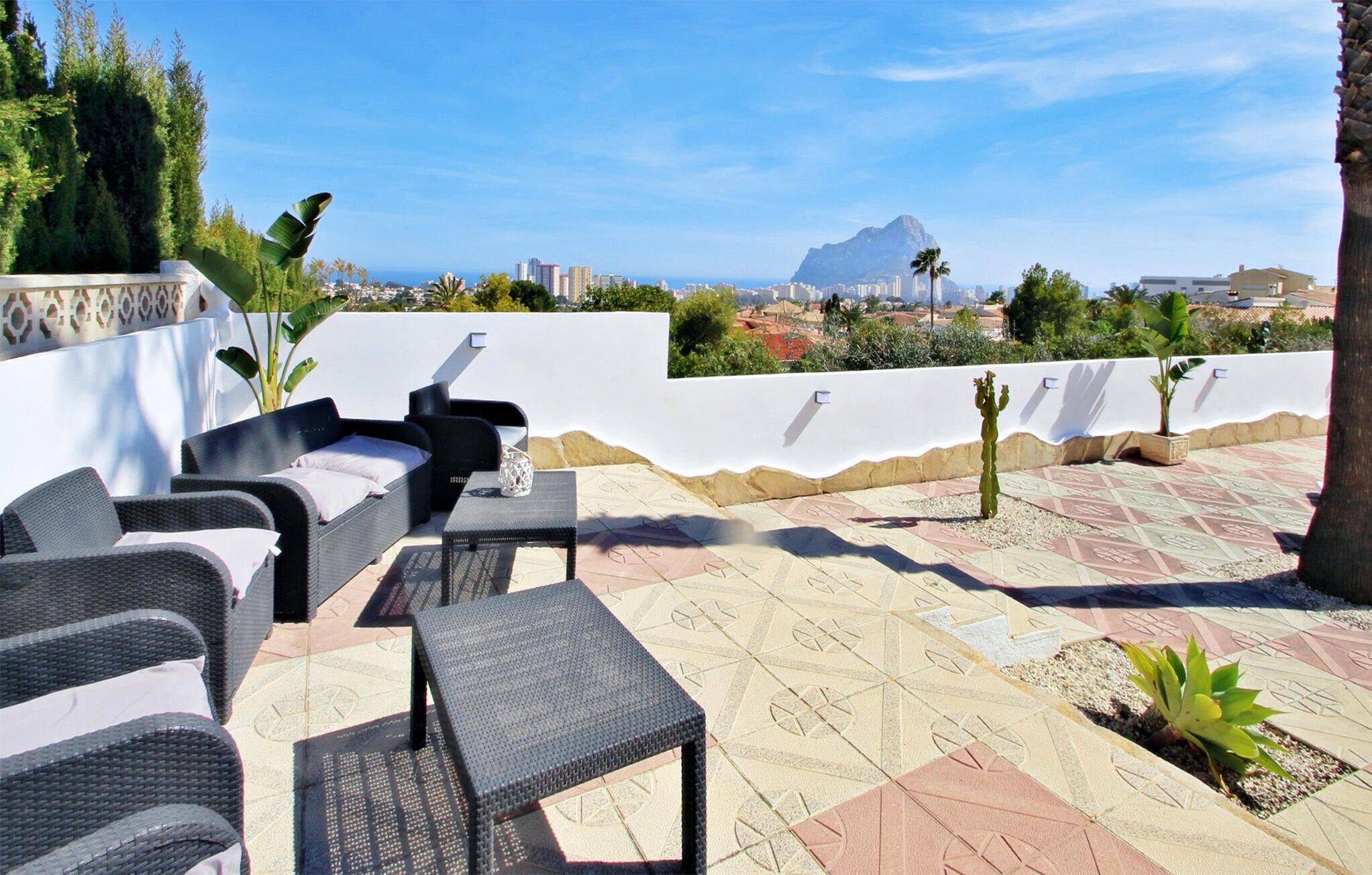 Una terrazza sul tetto con mobili da esterno, un cactus e vista su montagna e skyline urbano.