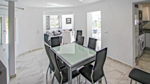 A modern dining area with a glass table and black chairs, a kitchen with a washing machine, and a view of the outdoors. - Stunning home in Benissa (Benissa)
