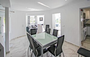 Ein moderner Essbereich mit Glastisch und schwarzen Stühlen, eine Küche mit Waschmaschine und Blick ins Freie.