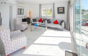 Ein stilvolles Wohnzimmer mit einer Couch, Sesseln, einem Couchtisch und einem großen Fenster mit Vorhängen.