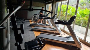 A gym with treadmills, weight machines, and a large window with greenery outside. - Grand Sungkono Lagoon Caspian Apartment 1BR (Surabaya)