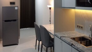 A modern kitchen with grey cabinets, a built-in microwave, and a dining area with a table and chairs. - Grand Sungkono Lagoon Caspian Apartment 1BR (Surabaya)