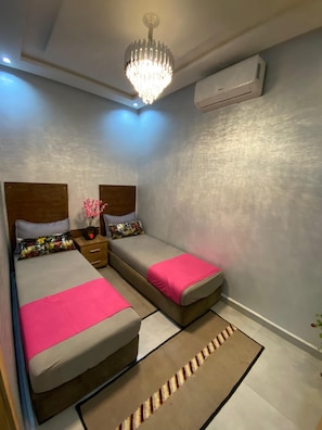 A bedroom with two beds, a chandelier, an air conditioner, and a patterned rug. - Luxury 2-bedroom apartment (Kénitra)