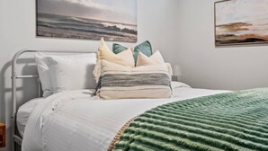 A bed with a green blanket, pillows, and a woven throw.