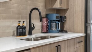 A kitchen with a stainless steel sink, a black faucet, a blue coffee maker, and two black bottles labeled 'HAND DISHES.'